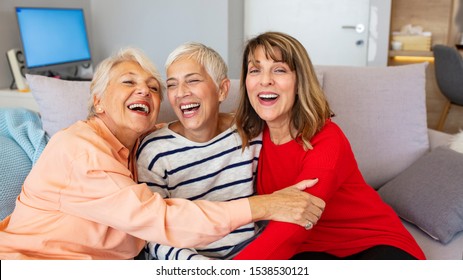 Portrait Of Three Retired Senior Female Friends Sitting On Sofa. Group Of Senior Female Friends Relaxing On Sofa At Home. Three Women In Living Room Talking And Smiling