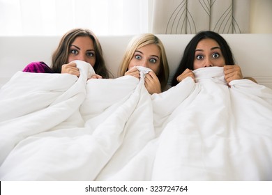 Portrait of a three scared girlfriends covering their face with blanket