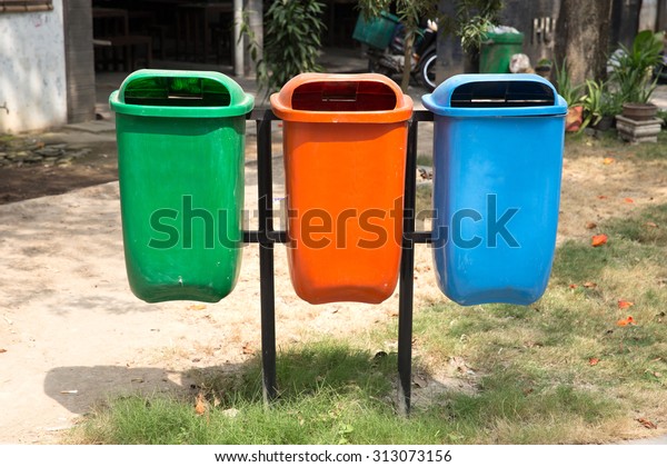 A portrait of three trash bin in different colors\
and purpose on a park