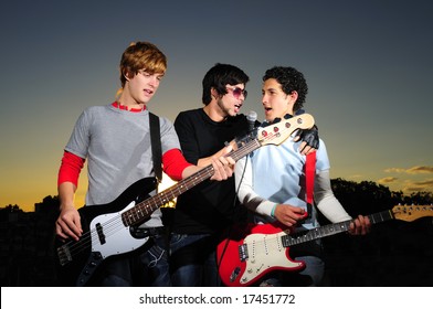 Portrait Of Three Trendy Teenagers Playing Music Outdoors