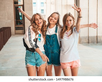 Portrait of three young beautiful smiling hipster girls in trendy summer clothes. Sexy carefree women posing on the street background.Positive models having fun.They raise hands