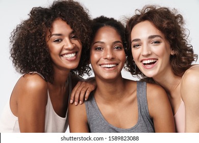 Portrait von drei jungen Frauen aus verschiedenen ethnischen Gruppen, die zusammenstehen und bei der Kamera lächeln, einzeln auf weißem Hintergrund