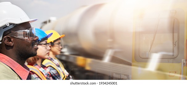 A portrait three-person team of petroleum depot engineers standing in line against the blurred background of a tanker train. The petroleum transportation industry by a rail system.