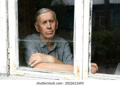 Portrait Through The Glass Window. A Sad Elderly Man Of 80 Years Old, Sitting In An Old House. 