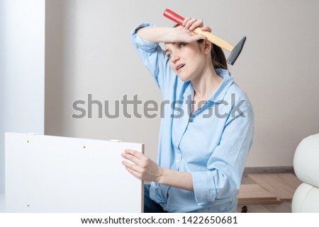 Portrait of a tired brunette woman with a hammer in her hands, wipes her forehead with sweat, furniture Assembly, copy space
