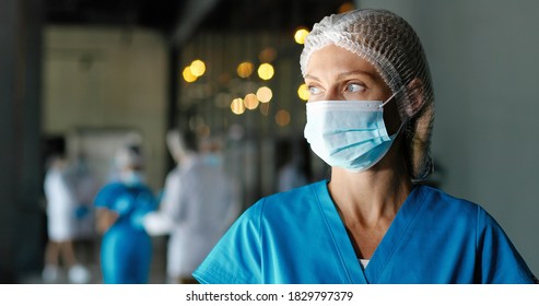 Portrait Of Tired Caucasian Pretty Woman Doctor In Hat And Medical Mask Looking At Camera. Close Up Of Female Physician. Medic Or Nurse In Clinic. Indoor. Coronavirus Concept. Protected.