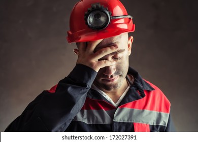 Portrait of tired coal miner holding hand his head against a dark background    - Powered by Shutterstock