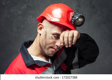 Portrait of tired coal miner wiping forehead his hand against a dark background - Powered by Shutterstock