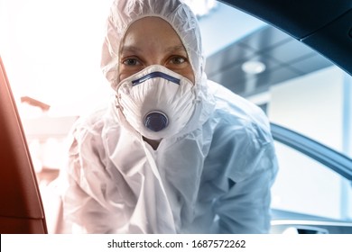 Portrait of tired exhausted female doctor, scientist or nurse wearing face mask and biological hazmat protective suit open car door on road outdoor. Coronavirus covid-19 outbreak alert danger
