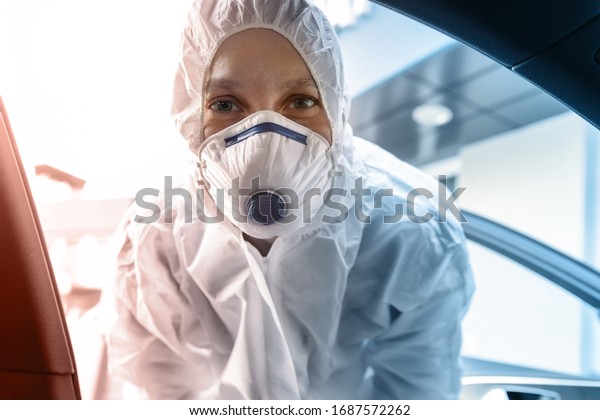 Portrait of tired exhausted female doctor,\
scientist or nurse wearing face mask and biological hazmat\
protective suit open car door on road outdoor. Coronavirus covid-19\
outbreak alert danger