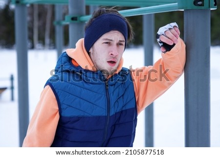 Portrait of tired exhausted man, young fit athletic guy is feeling bad, unwell after doing exercise training work out with horizontal bar outdoors at winter cold day in snow, having dyspnea, dizziness