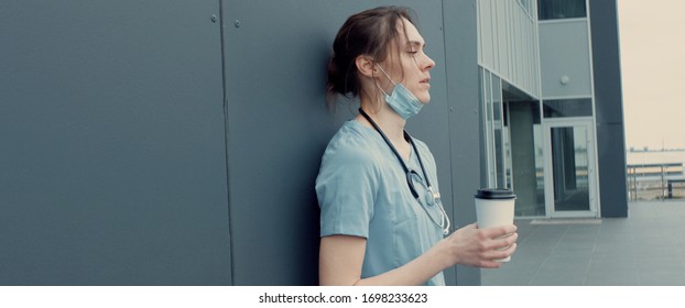 Portrait of tired exhausted nurse or doctor having a coffee break outside in the morning. COVID-19, Coronavirus pandemic