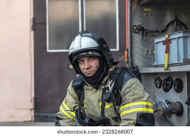 Portrait of a tired firefighter in a protective suit and a protective helmet sitting by a fire engine after returning to the fire department - Powered by Shutterstock