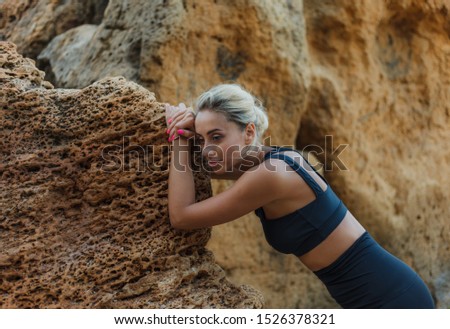 Portrait of a tired fitness woman in sportswear leaning on a stone on a wild beach. Outdoor training concept