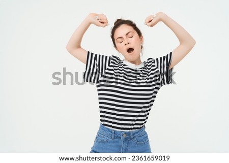 Portrait of tired girl yawning and stretching her arms. Lazy woman looking sleepy, standing over white background.
