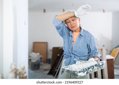 Portrait of tired mature woman holding tools for painting wall, need break while renovating home with her own hands - Powered by Shutterstock