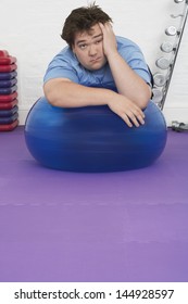 Portrait Of A Tired Overweight Man Resting On Exercise Ball In Health Club