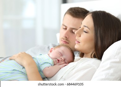 Portrait Of Tired Parents Sleeping With Their Baby On A Bed At Home