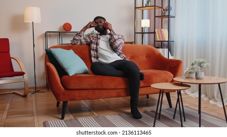 Portrait Of Tired Sleepy Man In Shirt Talking On Mobile Phone With Friend At Home. Sad African American Guy Freelancer Making Online Conversation Speaks On Smartphone Sitting On Sofa At Living Room