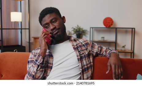 Portrait Of Tired Sleepy Man In Shirt Talking On Mobile Phone With Friend At Home. Sad African American Guy Freelancer Making Online Conversation Speaks On Smartphone Sitting On Sofa At Living Room