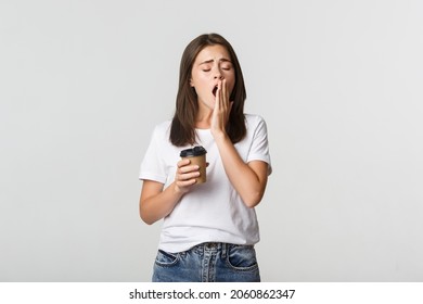 Portrait Of Tired And Sleepy Young Attractive Girl Yawning While Drinking Takeaway Coffee, White Background