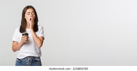 Portrait Of Tired And Sleepy Young Attractive Girl Yawning While Drinking Takeaway Coffee, White Background.