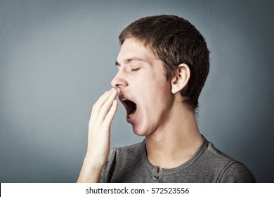 Portrait Of Tired Teen Who Yawns On A Gray Background