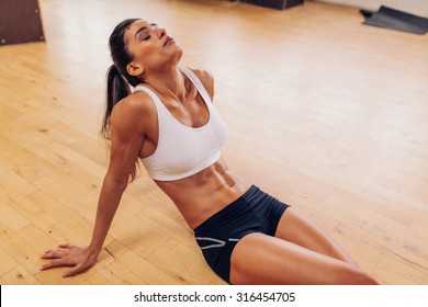 Portrait Of Tired Woman Having Rest After Workout. Tired And Exhausted Female Athlete Sitting On Floor At Gym.