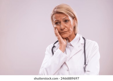 Portrait of tired and worried mature female doctor  on gray background. - Powered by Shutterstock