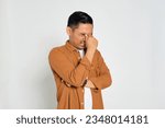 Portrait of tired young Asian man in casual shirt rubbing eyes with finger isolated on white background