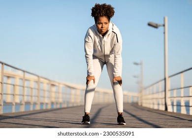 Portrait Of Tired Young Black Female Athlete Resting After Jogging Outdoors, Motivated African American Woman In Sportswear Catching Breath And Leaning On Knees, Taking Break During Morning Run - Powered by Shutterstock