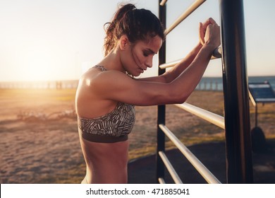 Portrait Of Tired Young Fitness Woman Leaning To Wall Bars Outdoors. Female Standing By Outdoor Fitness Equipment Taking A Break From Her Workout.