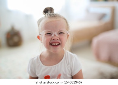 Portrait Of A Toddler Girl In Glasses With Down Syndrome In A Bright Room, Concept For Children With Disabilities And Visual Impairment