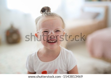 Portrait of a toddler girl in glasses with down syndrome in a bright room, concept for children with disabilities and visual impairment