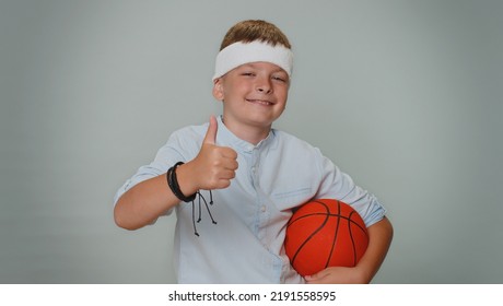 Portrait Of Toddler Kid Boy Sportsman Basketball Fan Holding Ball Looking At Camera, Training Dribbling. Young Teenager Child Schoolboy On Gray Background. Workout Sport Motivation Lifestyle Concept