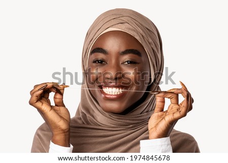 Portrait Of Toothy African American Muslim Woman In Hijab Flossing And Cleaning Teeth Using Tooth Floss In The Morning. Toothcare And Healthy Oral Hygiene Concept. White Studio Background