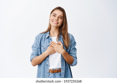 Portrait Of Touched Young Woman Feeling Flattered, Holding Hands On Heart And Smiling White Teeth, Say Thank You, Appreciate Help, Being Grateful For Nice Gesture, White Background