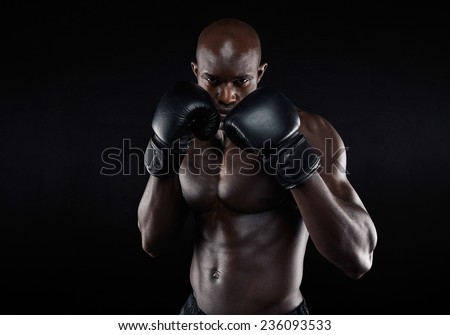 Portrait of tough male boxer posing in boxing stance against black background. Professional fighter ready for boxing match.