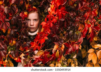 Portrait Of Tough Redhead Girl With Freckles Face Standing Inside Ivy Wall And Looking With Adult Face Expression.  