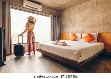 Portrait of tourist woman standing nearly window, looking to beautiful view with her luggage in hotel bedroom after check-in. Conceptual of woman lifestyle when traveling on her vacation.