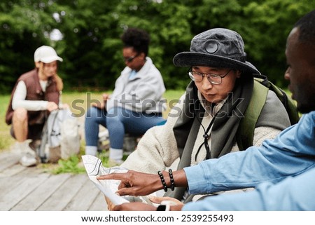 Portrait of tourists looking at map while exploring nature trails with multiethnic group of friends copy space