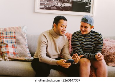 Portrait of trans couple sitting on couch looking at smartphone and talking - Powered by Shutterstock