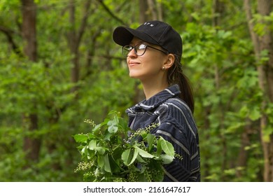 Portrait Of Traveler Smiling Young Woman In Black Cap And Glasses Breathing Fresh Air In The Green Spring Forest. Nature Background. Walking And Resting In Woodland.