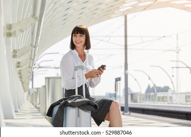 Portrait of traveling business woman waiting in terminal with suitcase and mobile phone - Shutterstock ID 529887046