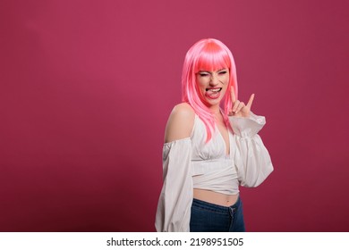 Portrait Of Trendy Carefree Woman Doing Rock Sign And Sticking Tongue Out, Showing Aggressive Hipster Devil Gesture. Cool Female Rocker Advertising Funky Heavy Metal Symbol, Fooling Around.