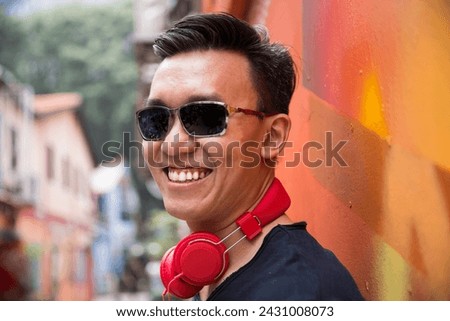 Portrait of a trendy Chinese man leaning against an urban wall outdoors.