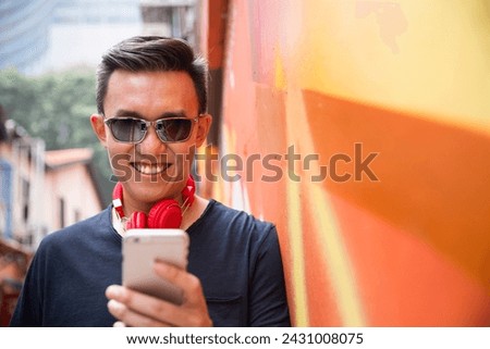 Portrait of a trendy Chinese man leaning against a wall using his smart phone.