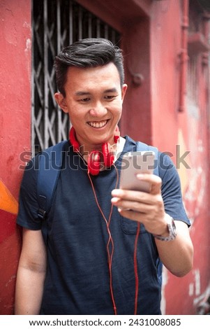 Portrait of a trendy Chinese man leaning against a wall using his smart phone.