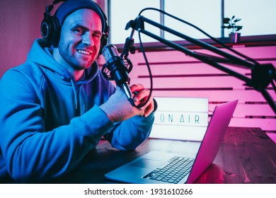 Portrait of trendy podcast creator streaming audio broadcast at his home studio using stylish cyber punk ambient light