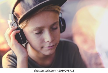 Portrait Of A Trendy Teen Enjoying The Sound With Headphones. Beautiful Boy With Earphones And Rapper Hat Relax Listening Music.  Teenager Playing His Rock Playlist. Youth, Recreation, Fun Concept.